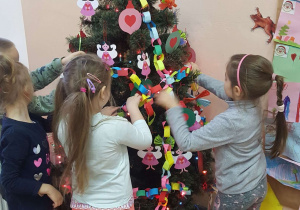 Przedszkolaki dekorują łańcuchem choinkę.